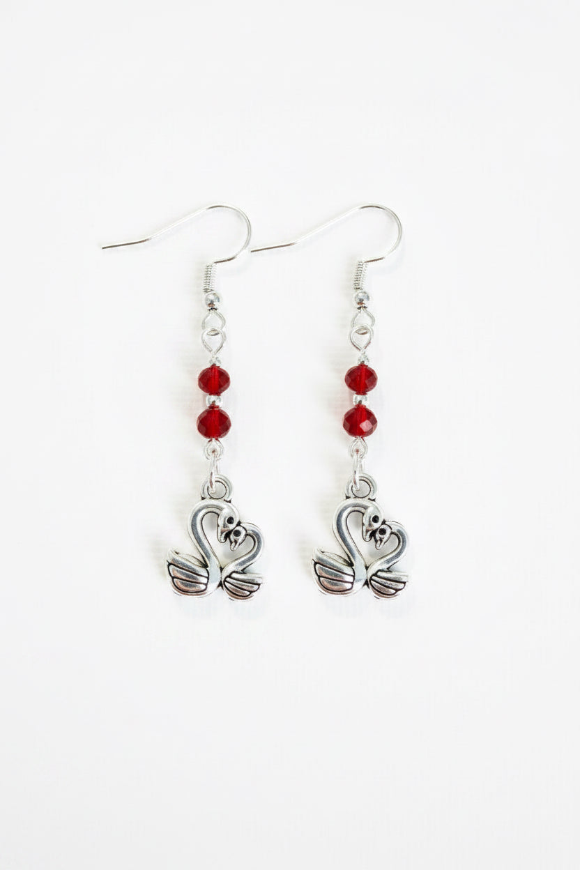 A pair of silver-toned dangle earrings with three small red faceted beads and a swan-shaped charm at the bottom, shown on a plain white background.