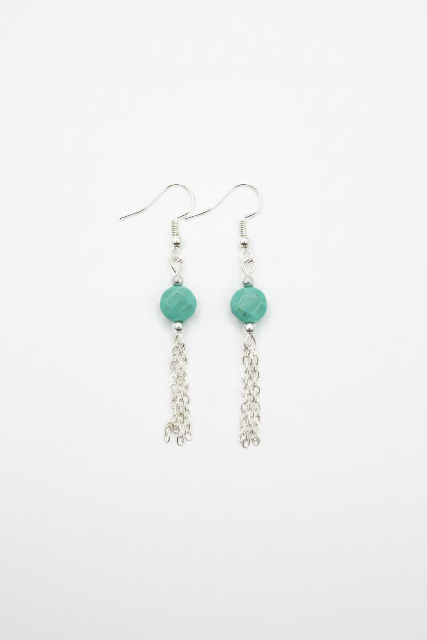 A pair of silver dangle earrings with faceted green beads and dangling chain links, shown on a plain white background.