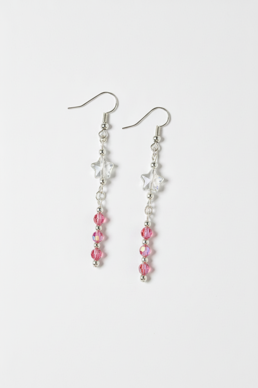 A pair of silver dangle earrings featuring a white star charm, a clear faceted bead, and a vertical strand of pink faceted beads on a light gray background.