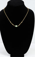 A delicate gold chain necklace with a single light green oval stone pendant, displayed on a black velvet jewelry bust against a white background.