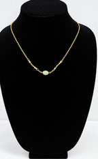 A delicate gold chain necklace with a single light green oval stone pendant, displayed on a black velvet jewelry bust against a white background.