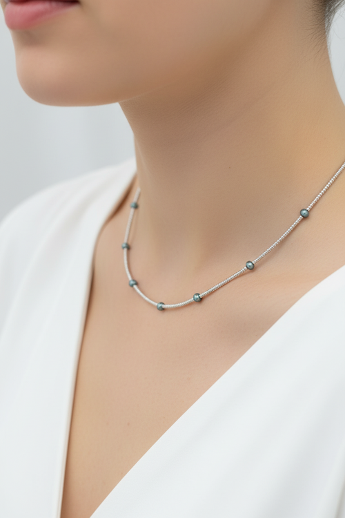 Necklace with small beads worn by a person on a plain background