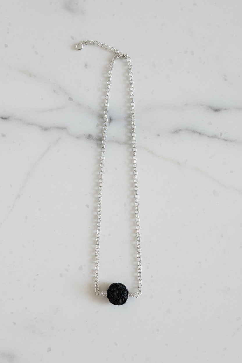 Silver necklace with a black pendant on a marble surface