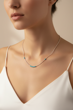 Necklace with small green beads worn by a model in a white top against a beige background