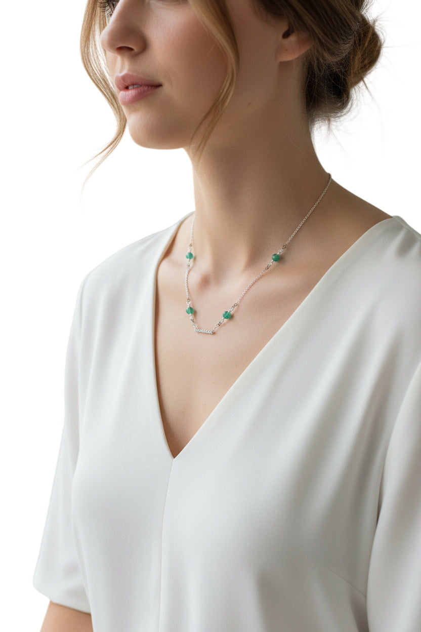 Woman wearing a delicate necklace with green gemstones against a neutral background
