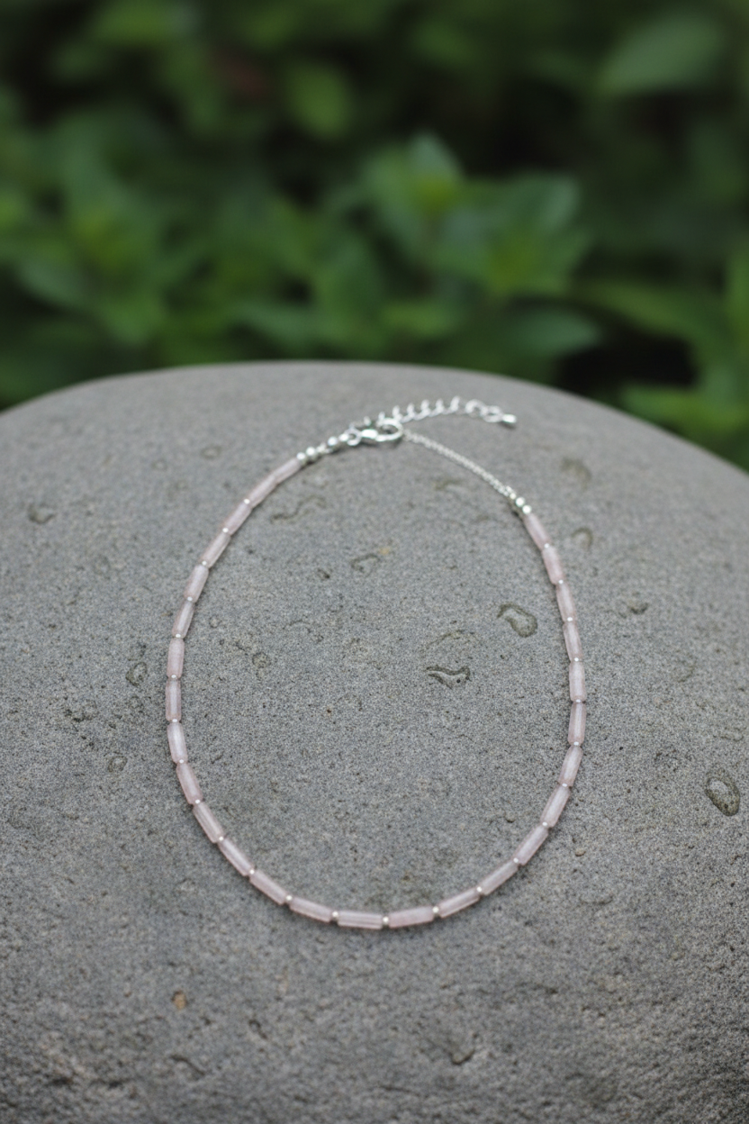 Silver beaded necklace on a gray stone with green foliage in the background
