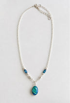 A silver chain necklace featuring a teardrop-shaped blue pendant and two smaller blue beads, displayed on a light gray background.