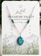 Treasure Valley Creations necklace featuring a blue oval pendant and silver chain with blue beads, displayed on its illustrated white backing card.
