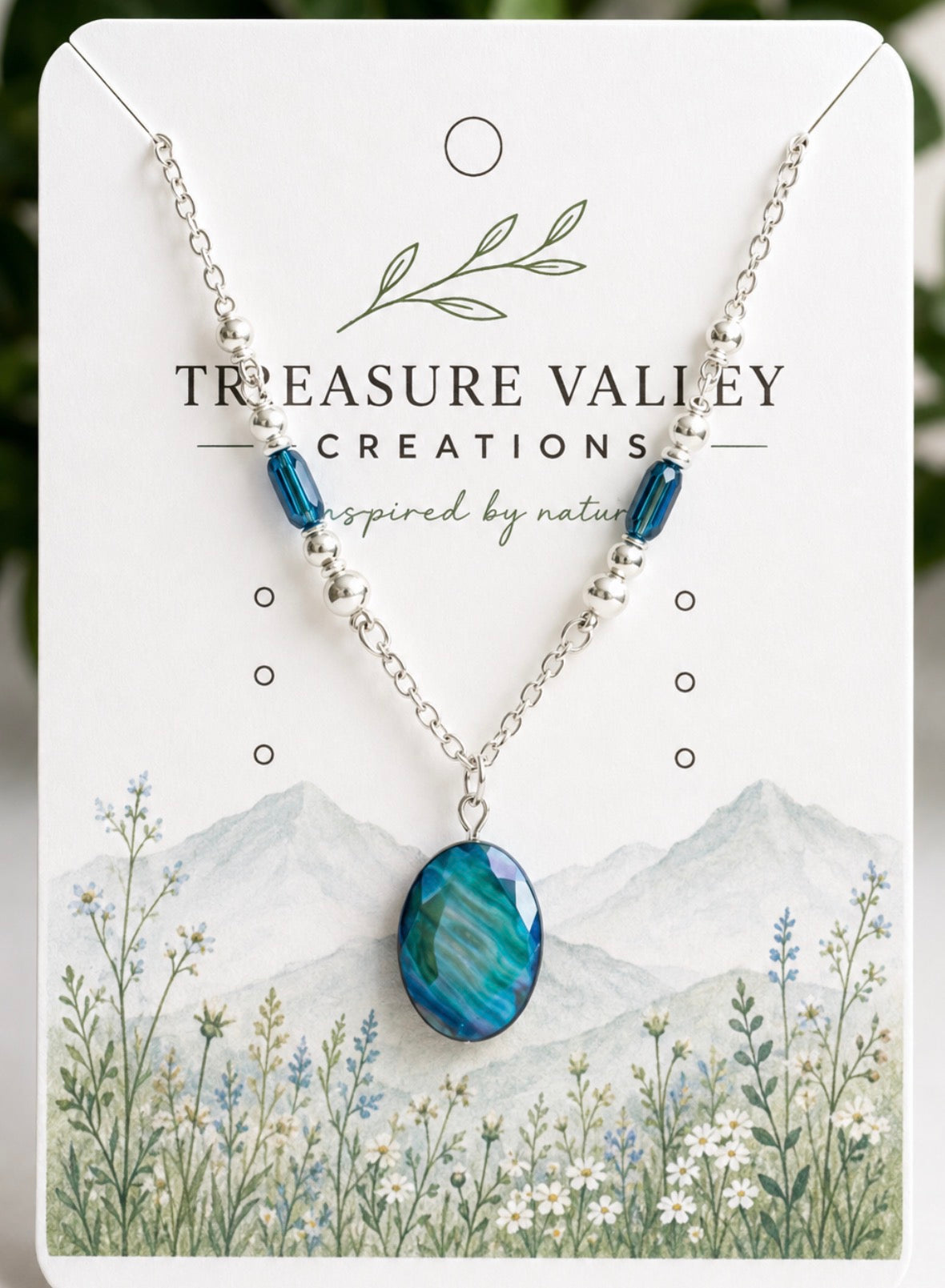Treasure Valley Creations necklace featuring a blue oval pendant and silver chain with blue beads, displayed on its illustrated white backing card.